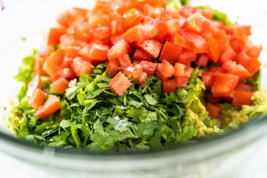 Mixing ingredients in a glass mixing bowl to prepare classic guacamole dip on the counter.