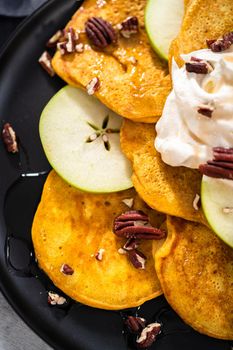 Freshly made pumpkin pancakes with green apples on a black serving plate.