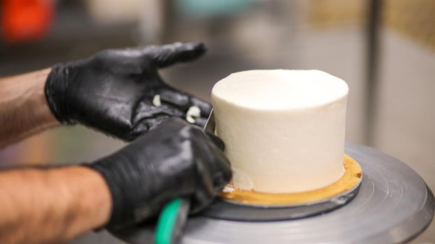 Decorator using spatula and scraper to smooth buttercream on a frosted cake