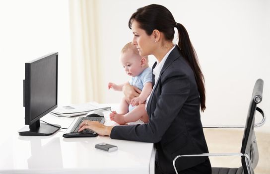 Daycare is indispensable to a working mom. Working mother holding a baby while working on her computer - copyspace
