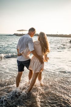 Summer holidays and travel. Sexy woman and man in sea water at sunset. Loving couple relax on the sunrise beach. Love relationship of a couple enjoying a summer day together