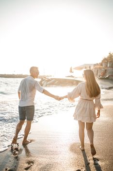 A couple in love is walking on the beach near the sea. Young family at sunset by the mediterranean sea. Summer vacation concept