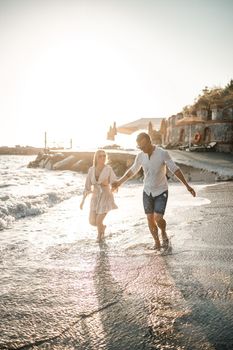 A couple in love is walking on the beach near the sea. Young family at sunset by the mediterranean sea. Summer vacation concept