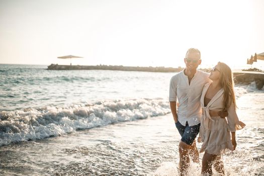 A couple in love is walking on the beach near the sea. Young family at sunset by the mediterranean sea. Summer vacation concept