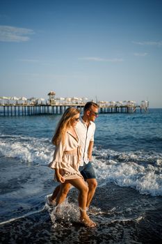 romantic young couple in love together on the sand walks along the beach of the Mediterranean sea. Summer vacation in a warm country.