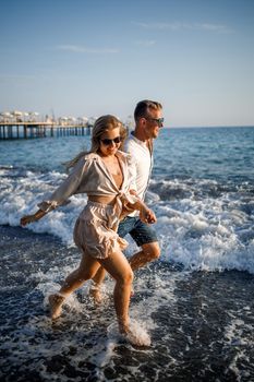 romantic young couple in love together on the sand walks along the beach of the Mediterranean sea. Summer vacation in a warm country.