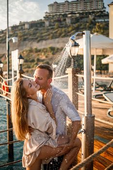 Happy couple by the sea. A guy and a girl are under the shower on an open-air pier. Happy couple on vacation. Man and woman by the sea.