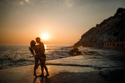 Beautiful couple in love on the background of the sunset by the sea. Young woman and man hugging by the sea at sunset