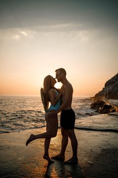 Beautiful couple in love on the background of the sunset by the sea. Young woman and man hugging by the sea at sunset