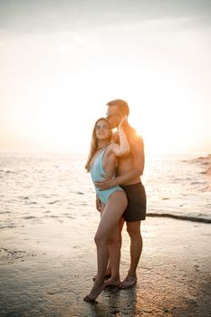 A loving couple walks along the beach by the sea. Young family at sunset by the Mediterranean Sea. Vacation concept. A woman in a swimsuit and a man in shorts at sunset by the sea. Selective focus.