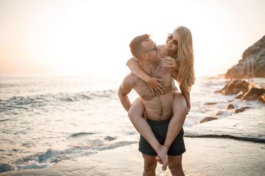 A loving couple walks along the beach by the sea. Young family at sunset by the Mediterranean Sea. Vacation concept. A woman in a swimsuit and a man in shorts at sunset by the sea. Selective focus.