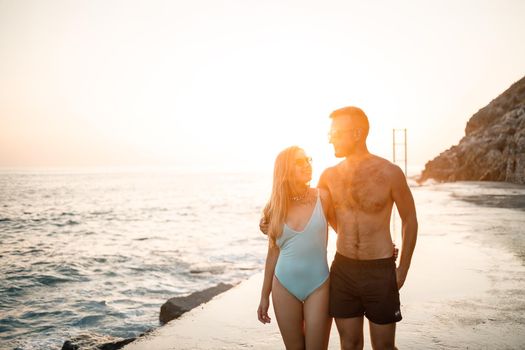 Romantic young couple in love walking together at sunset along the Mediterranean beach. Summer vacation in a warm country. Happy married couple on vacation in Turkey. Selective focus