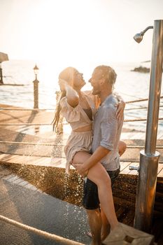 Happy couple by the sea. A guy and a girl are under the shower on an open-air pier. Happy couple on vacation. Man and woman by the sea.