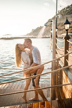 Happy couple by the sea. A guy and a girl are under the shower on an open-air pier. Happy couple on vacation. Man and woman by the sea.