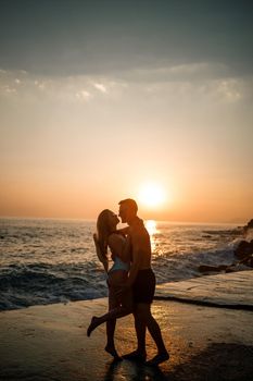 Beautiful couple in love on the background of the sunset by the sea. Young woman and man hugging by the sea at sunset