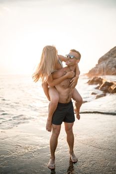 A loving couple walks along the beach by the sea. Young family at sunset by the Mediterranean Sea. Vacation concept. A woman in a swimsuit and a man in shorts at sunset by the sea. Selective focus.