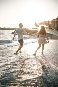 A couple in love is walking on the beach near the sea. Young family at sunset by the mediterranean sea. Summer vacation concept. Selective focus