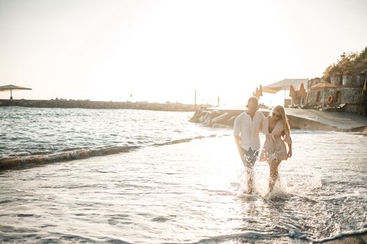 A couple in love is walking on the beach near the sea. Young family at sunset by the mediterranean sea. Summer vacation concept