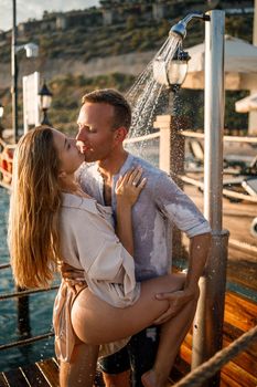 Happy couple by the sea. A guy and a girl are under the shower on an open-air pier. Happy couple on vacation. Man and woman by the sea.