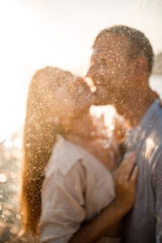 Beautiful couple in love hugs and kisses under the streams of water in a luxury spa hotel on their honeymoon, vacation in the tropics. Selective focus