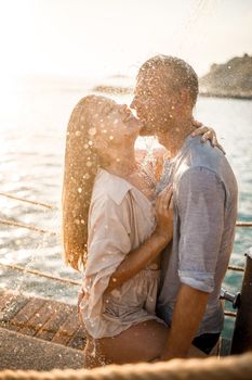 Beautiful couple in love hugs and kisses under the streams of water in a luxury spa hotel on their honeymoon, vacation in the tropics. Selective focus