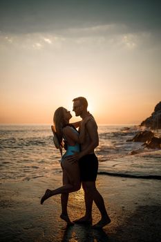 Beautiful couple in love on the background of the sunset by the sea. Young woman and man hugging by the sea at sunset