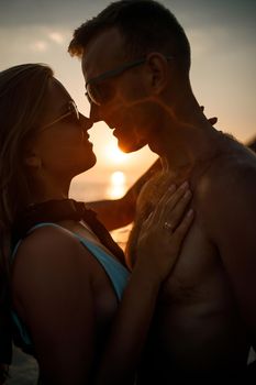 Beautiful couple in love on the background of the sunset by the sea. Young woman and man hugging by the sea at sunset