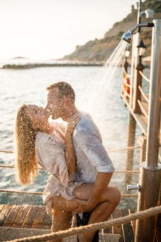 Happy couple by the sea. A guy and a girl are under the shower on an open-air pier. Happy couple on vacation. Man and woman by the sea.