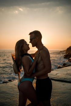 Beautiful couple in love on the background of the sunset by the sea. Young woman and man hugging by the sea at sunset