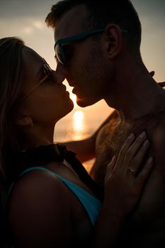 Beautiful couple in love on the background of the sunset by the sea. Young woman and man hugging by the sea at sunset