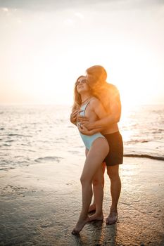 A loving couple walks along the beach by the sea. Young family at sunset by the Mediterranean Sea. Vacation concept. A woman in a swimsuit and a man in shorts at sunset by the sea. Selective focus.