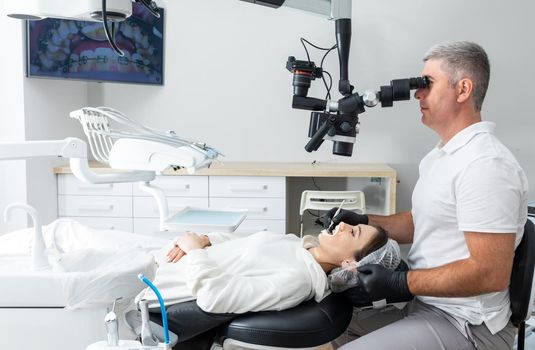 Male dentist using dental microscope treating patient teeth at dental clinic office. Medicine, dentistry and health care concept