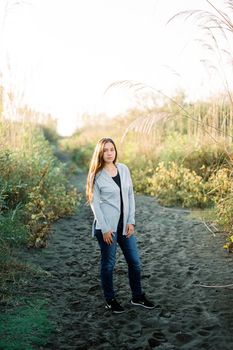Young woman in a long sweater stands on a sandy road in the park. High quality photo