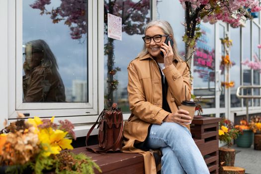 Stylish business elderly woman talking on a mobile phone Sitting on a bench next to a flower shop.