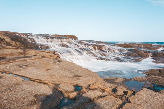 Milky ocean cascades flowing over honey coloured rocks.  Australia
