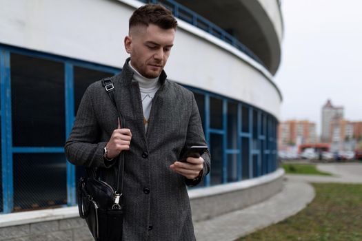 young man with a mobile phone and a business bag on the background of a parking lot.