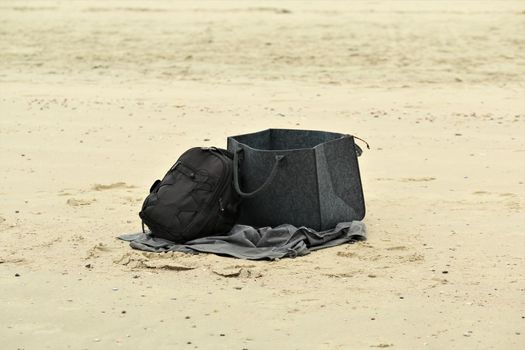 One black backpack and a grey big bag at the beach