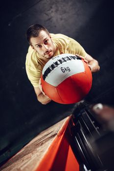 Handsome young muscular man doing exercise with wall ball at the gym. Top view. Looking at camera.