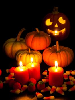 Lit orange candles with small pumpkins and jack-o'-lantern on black background.