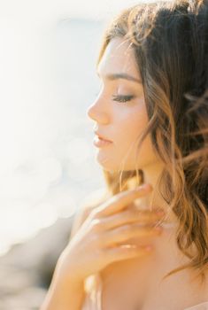 Bride in a beige dress touches her neck with her hand. Side view. Portrait. High quality photo