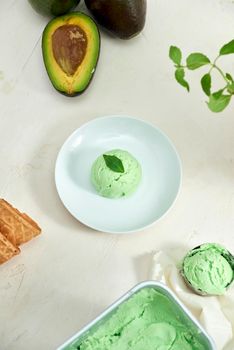 Avocado ice cream balls on a white plate, a spoon on a white background.