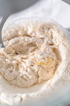 Mixing ingredients in a large glass mixing bowl to pizza dough.