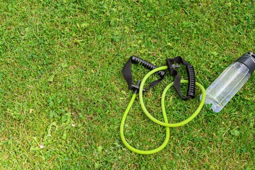 Fit tube and water bottle on the green grass background, top view. Outdoor training concept. Copy-space.