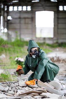 A man in a raincoat and gas mask collects a flower from a scorched, toxic land. Air pollution concept. Ecological catastrophy.