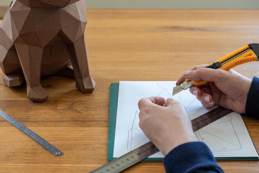 Somebody is making a cube sculpture with paper, linear and knife. DIY.