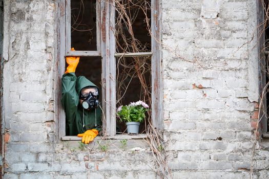 A woman in a raincoat and gas mask collects a flower from a scorched, poisonous earth. Air pollution concept. Ecological catastrophy.