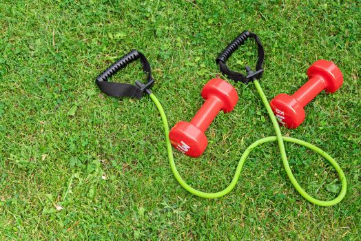 Ladie's dumbbells and fit tube the green grass background, top view. Outdoor training concept. Copy-space.