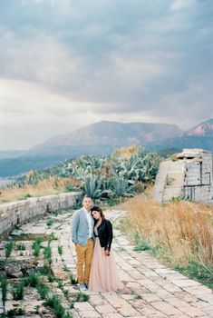 Bride and groom stand, holding hands, on the stone road. High quality photo