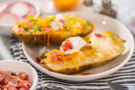Pressure Cooker Baked Potatoes. Garnished large baked potatoes with butter, sour cream, cheese, and bacon bits on a white plate.