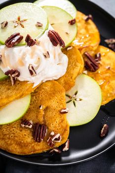 Freshly made pumpkin pancakes with green apples on a black serving plate.